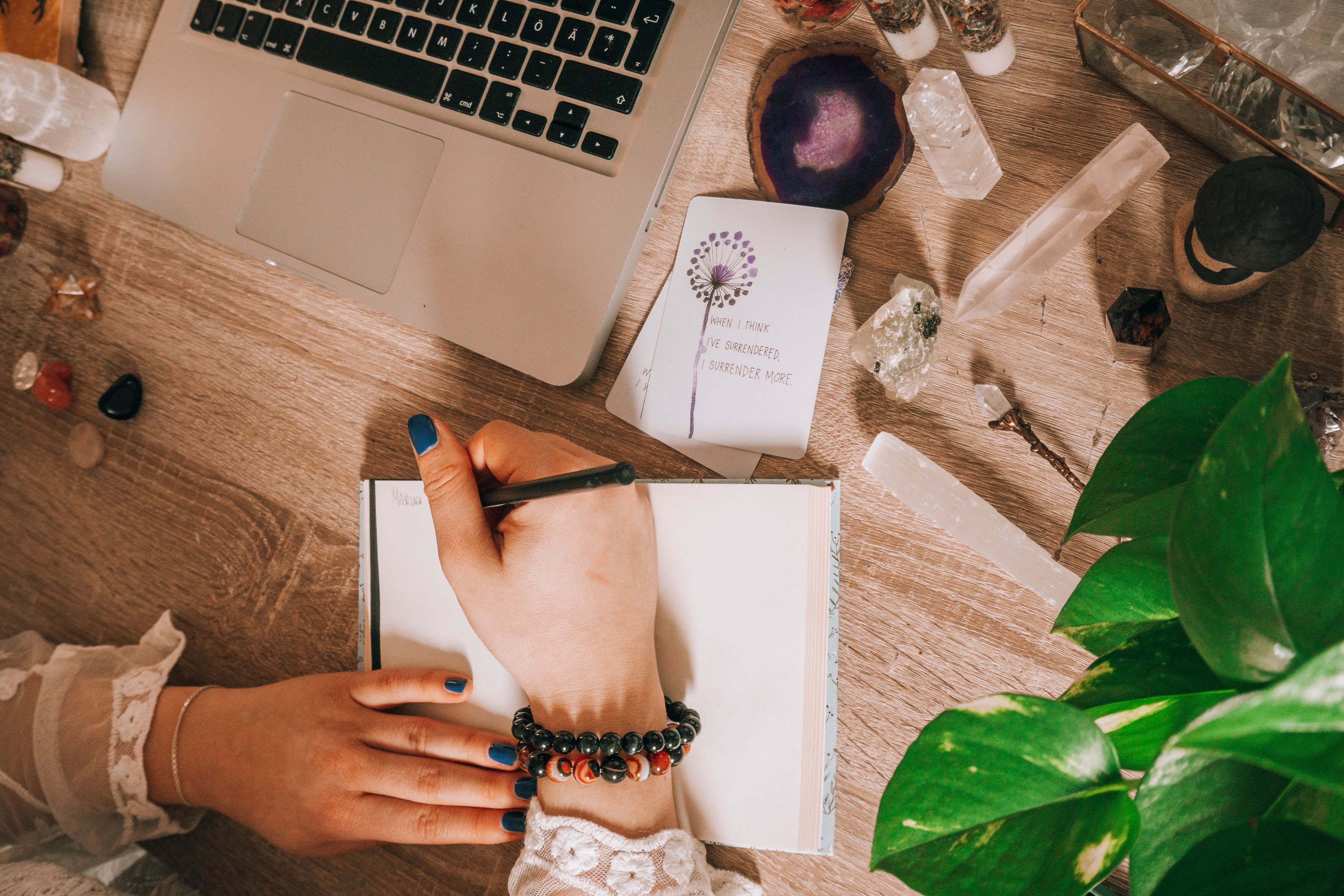 A reader writing beside cards, crystals, and a laptop